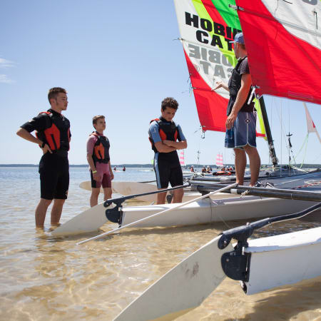 Groupe d'adolescents en stage de voile à Bénodet préparant des catamarans avec voiles colorées en bord de plage