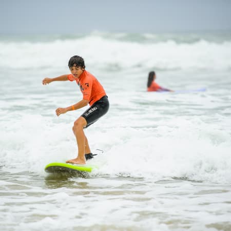 Jeune surfeur en équilibre sur sa planche verte dans les vagues avec un moniteur en arrière-plan