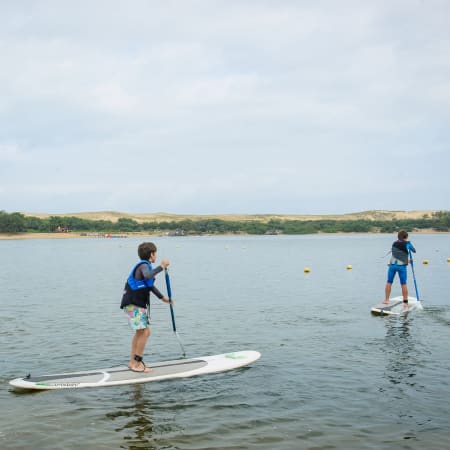 Enfants en cours de surf et paddle sur l'eau à Soustons, moniteur accompagnant les jeunes pratiquants sur planches blanches