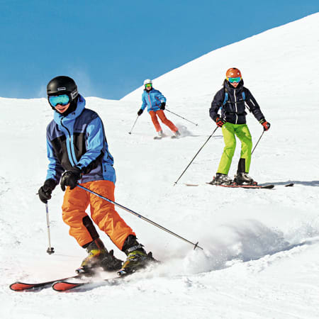 Groupe de skieurs en descente sur piste enneigée avec équipement de ski alpin et casques de protection