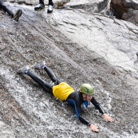 Jeune participant en canyoning escaladant une paroi rocheuse avec casque de protection et équipement de sécurité