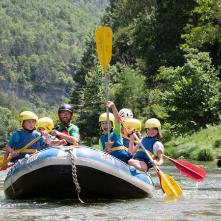 Groupe d'adolescents en rafting sur rivière avec gilets de sauvetage et casques, pagaies jaunes, forêt verte en arrière-plan