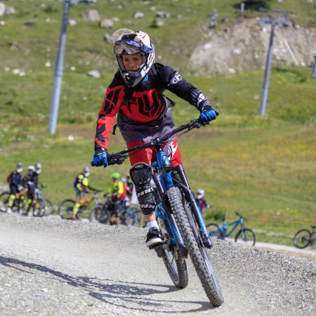 Jeune pilote en VTT de descente sur piste du Bike Park des Arcs avec groupe de riders en arrière-plan