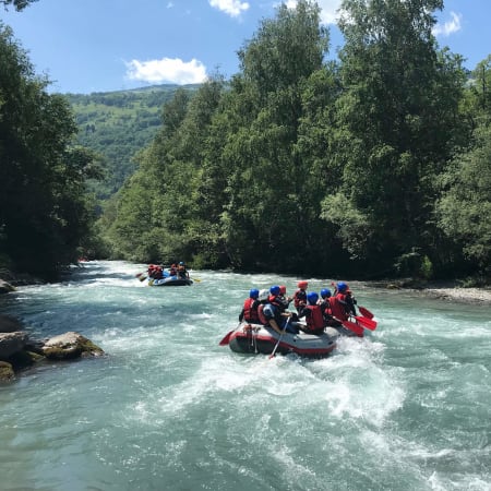 Enfants en rafting sur une rivière turquoise des Pyrénées entourée de forêts verdoyantes lors d'une activité de colo aventure
