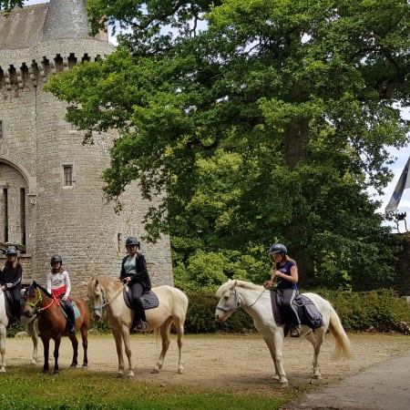 Groupe d'enfants à cheval devant un château médiéval en pierre, découverte équitation en nature