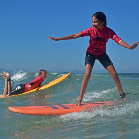 Moniteur de surf en équilibre sur sa planche face à l'océan guidant deux enfants en apprentissage du surf
