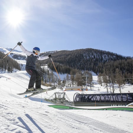 Jeune skieur en freestyle effectuant un saut au-dessus d'une rampe aux Orres, paysage montagneux enneigé en arrière-plan
