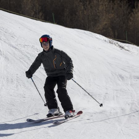 Jeune skieur débutant en tenue noire et casque rouge descendant une piste enneigée à Saint-Lary
