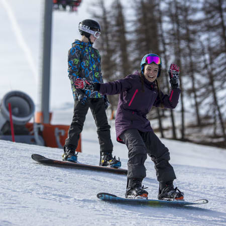 Adolescents skiant aux Orres durant un séjour initié à expert, en tenue de ski colorée et casque de protection sur piste enneigée