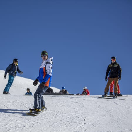 Groupe d'adolescents skiant et pratiquant le snowboard sur les pistes enneigées des Orres par beau temps