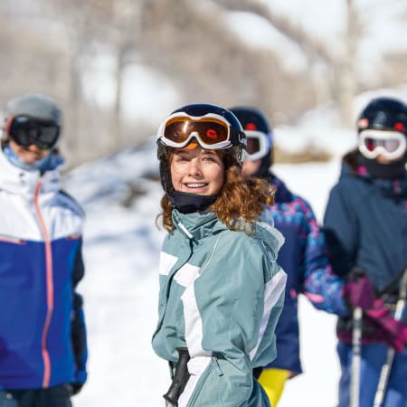 Jeune skieuse souriante en tenue all mountain avec ses camarades dans les Alpes enneigées
