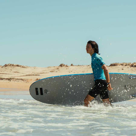 Jeune surfeur portant sa planche dans l'océan lors d'une séance de surf en bord de plage