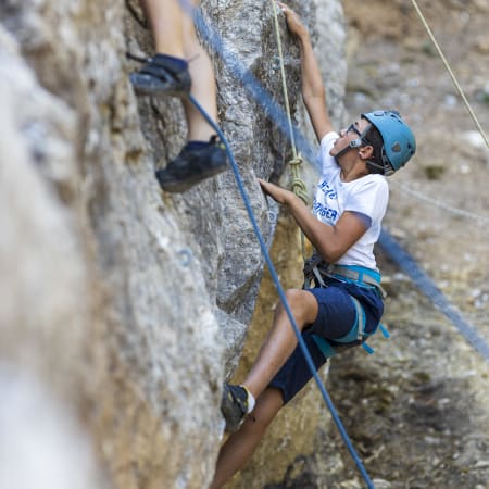 Jeune adolescent en escalade sportive équipé d'un casque bleu et d'une corde de sécurité sur une paroi rocheuse
