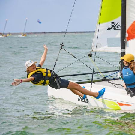 Deux navigateurs en gilet de sauvetage manœuvrant un catamaran avec voile verte et orange en mer peu profonde