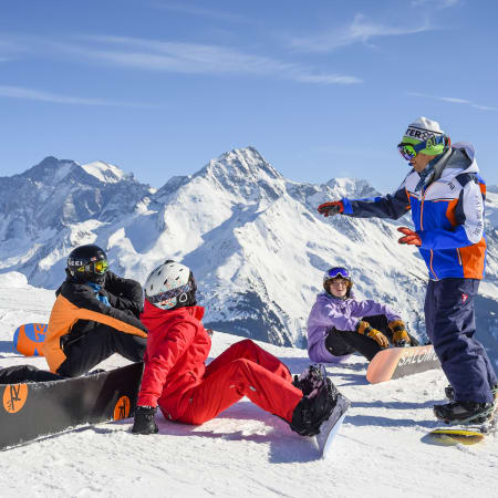 Groupe de jeunes snowboardeurs en pause sur un glacier avec montagnes enneigées aux Arcs