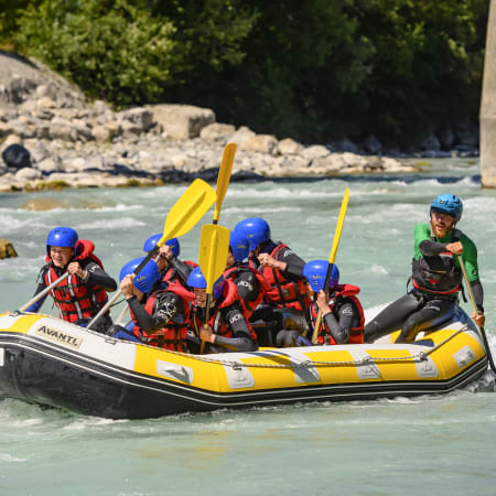 Groupe de jeunes en rafting dans les eaux vives alpines avec gilets de sauvetage et casques bleus