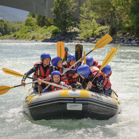 Groupe d'adolescents en rafting sur eaux vives alpines avec pagaies jaunes et gilets de sauvetage bleus