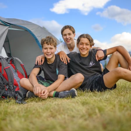 Trois jeunes en séjour multisports en Corse assis devant une tente de camping avec sacs à dos en montagne