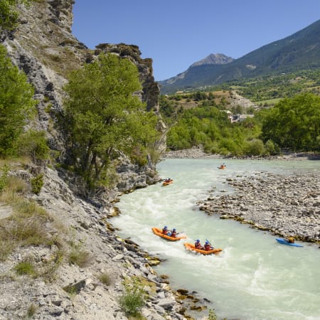 Kayakistes naviguant sur les eaux turquoise de la Durance à Embrun avec falaises rocheuses et sommets alpins en arrière-plan