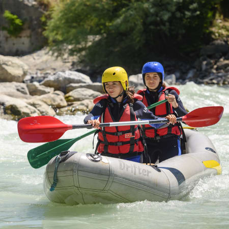 Deux jeunes en rafting dans les eaux vives alpines avec casques et gilets de sauvetage colorés