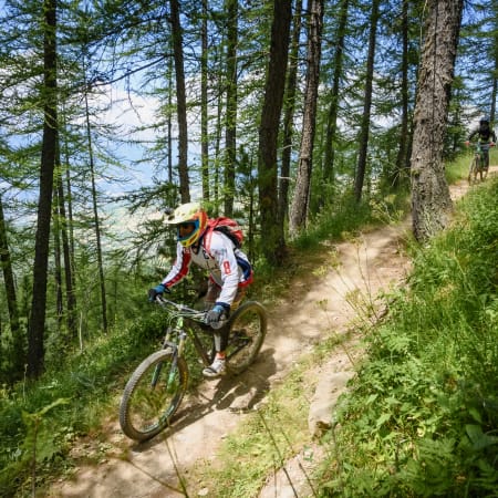Cycliste en VTT descendant un sentier sinueux en forêt au Bikepark des Arcs, initiation techniques de base