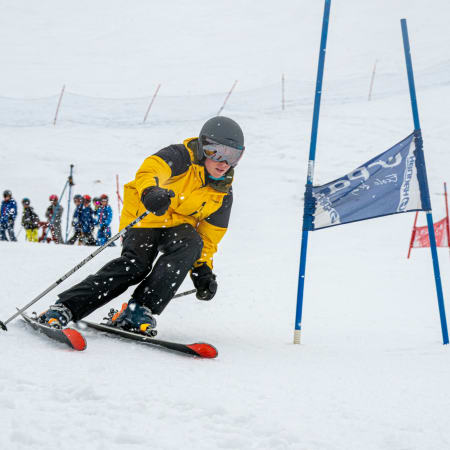 Jeune skieur en compétition franchissant une porte de slalom aux Arcs avec groupe de skieurs en arrière-plan