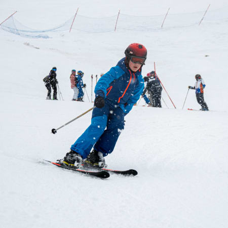 Jeune skieuse en tenue bleue dévale une piste aux Arcs avec d'autres apprentis skieurs en arrière-plan lors d'un cours collectif