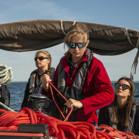 Adolescents en stage de voile niveau 3 FFV maniant cordages et voiles sur un bateau en mer bretonne