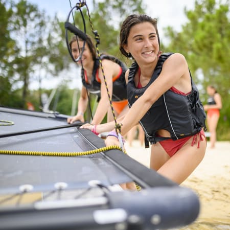 Jeune fille en gilet de sauvetage préparant son équipement de wakeboard sur la plage lors d'un séjour multisports nautiques