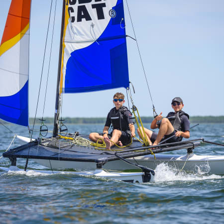 Enfants naviguant en catamaran avec voiles bleues et orange sur le Golfe du Morbihan lors d'un séjour multisports