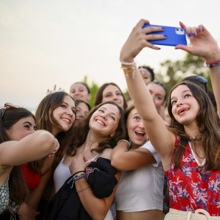 Groupe d'adolescents en Corse prenant un selfie collectif avec un smartphone bleu, sourires joyeux et paysage naturel en arrière-plan