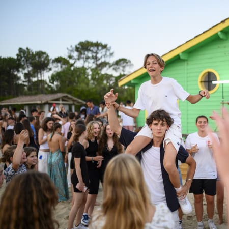 Adolescents en activité multisports nautique à Bombannes, garçon porté sur les épaules devant cabane colorée verte et jaune