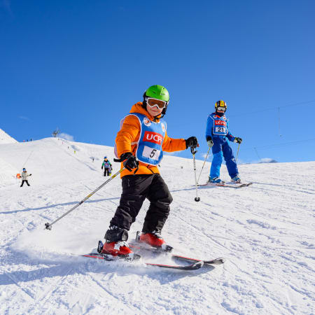 Enfant en tenue de ski orange et casque vert dévale une piste enneigée à La Plagne lors d'un séjour ski pour jeunes skieurs