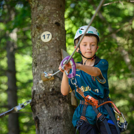 Enfant équipé de casque et harnais pratiquant l'escalade en forêt sur parcours d'aventure multisports