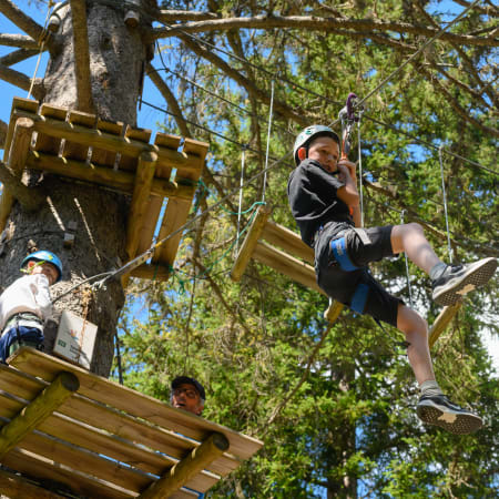 Enfant en parcours acrobatique dans les arbres à Pralognan, suspendu à une corde avec équipement de sécurité