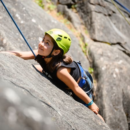 Enfant en escalade sur paroi rocheuse avec casque de sécurité jaune et équipement d'assurage