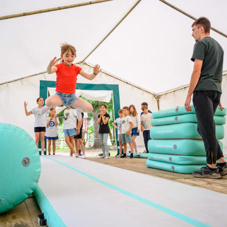 Enfant sautant sur un parcours de multisports en salle avec animateur et groupe d'enfants regardant