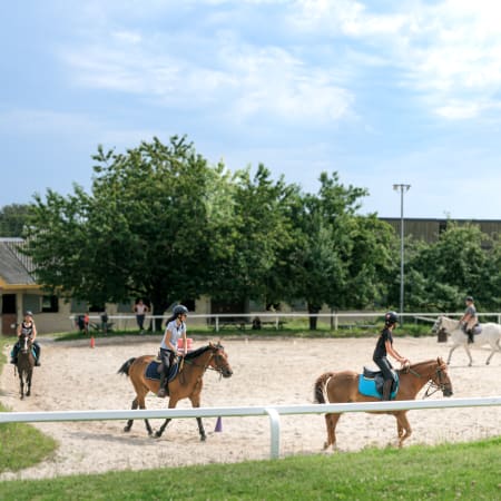 Jeunes cavaliers en séjour équestre à Quimper, montant à cheval dans un manège avec installations équestres en arrière-plan