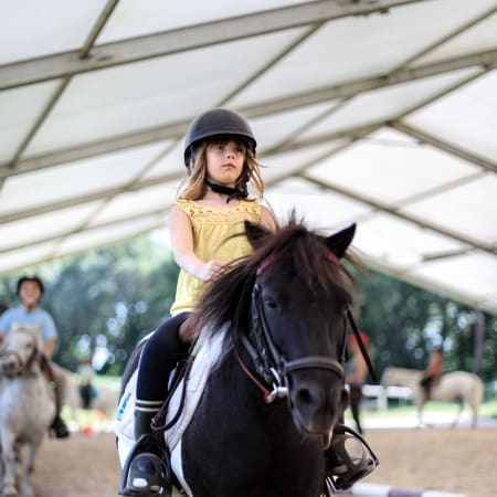 Enfant montant un poney noir avec casque d'équitation lors d'un stage équestre en Bretagne