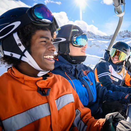 Trois jeunes skieurs et snowboardeurs souriants à Tignes avec des montagnes enneigées en arrière-plan