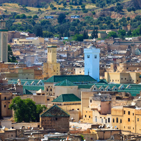 Panorama de la médina de Fès avec mosquée aux toits verts, minaret bleu et architecture traditionnelle marocaine