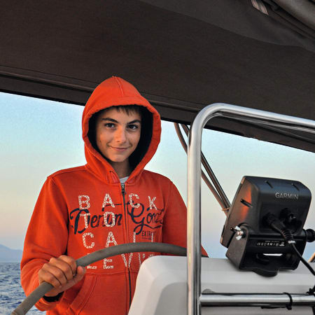 Adolescent en sweat-shirt rouge tenant une pagaie sur un bateau de croisière en Martinique