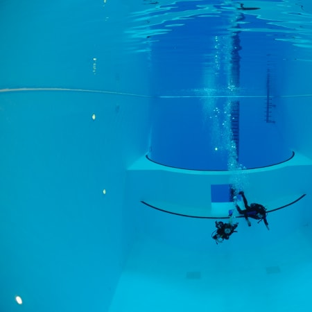 Plongeurs en formation sous une structure d'entraînement en piscine, équipés de bouteilles et détendeurs