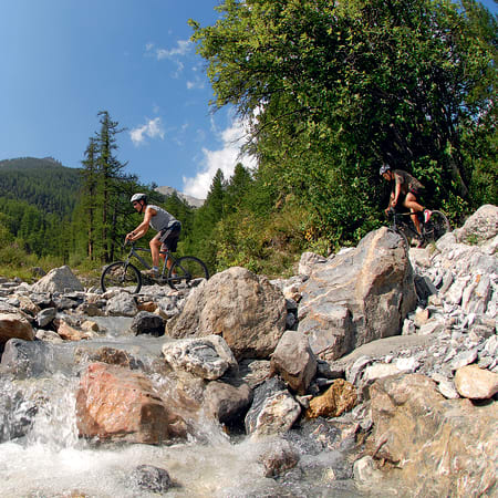 Cyclistes en VTT traversant un terrain rocheux avec montagnes et forêts en arrière-plan lors du raid Objectif Méditerranée