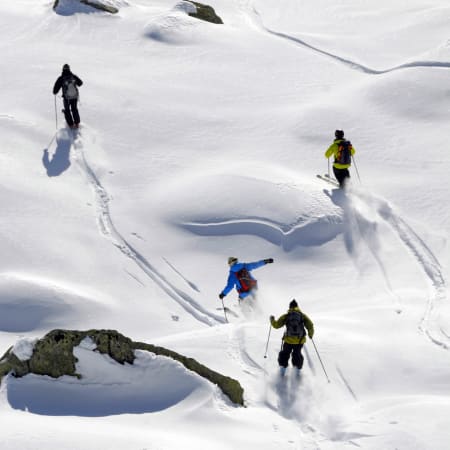 Skieurs en action dévalant des pentes enneigées hors-piste avec crevasses et reliefs montagneux