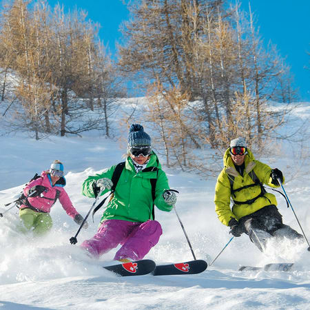 Skieurs en freerando dévallant une pente vierge enneigée avec mélèzes dorés et ciel bleu en arrière-plan