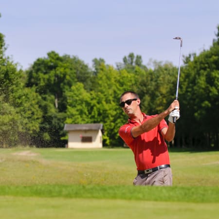Golfeur en polo rouge frappant un coup de golf sur un parcours ensoleillé avec arbres en arrière-plan