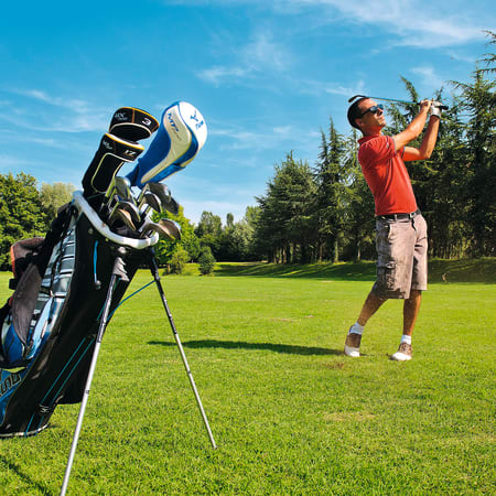 Golfeur en polo rouge exécutant un swing sur un parcours de golf verdoyant avec sac de clubs au premier plan