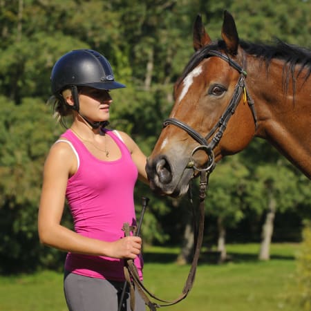 Cavalière en tenue de sécurité avec son cheval bai dans un centre équestre en forêt