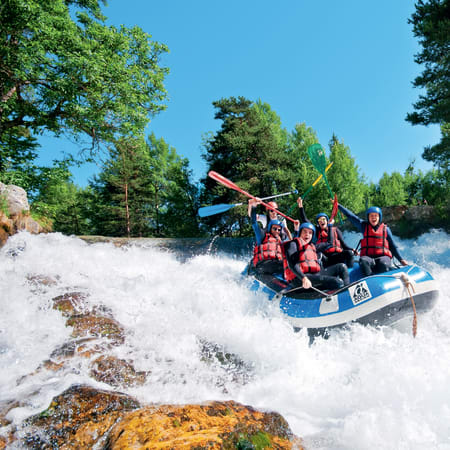 Groupe en rafting sur rapides écumants entouré de forêts des Hautes Alpes, gilets de sauvetage rouge et bleu